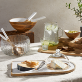 Table setting with wooden bowls, glassware, and a cheese platter.