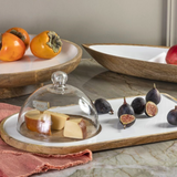 Fruits and cheese on a marble surface with a glass dome cover.