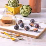 Figs on a white tray with artichokes and a yellow container in the background.
